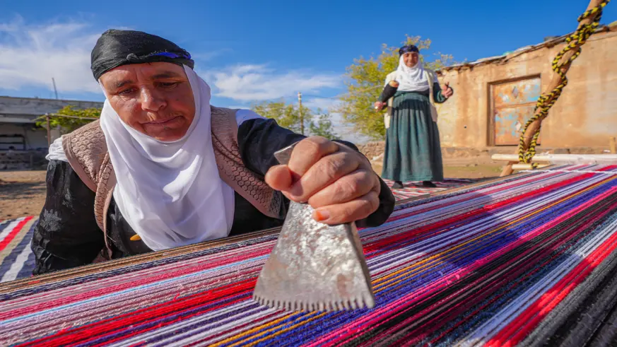 Evinin bahçesindeki tezgahta asırlık yöntemle kilim dokuyor